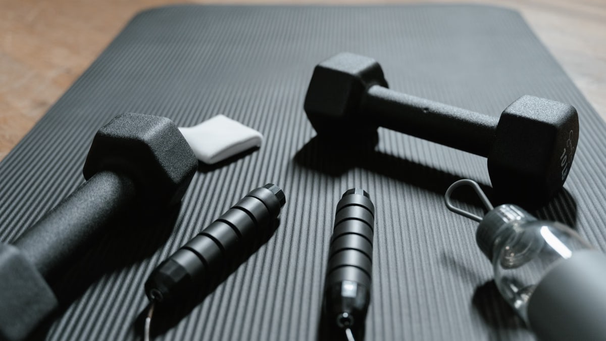 Close-up of dumbbells, jump rope, and water bottle on a yoga mat, ideal for home fitness routines.